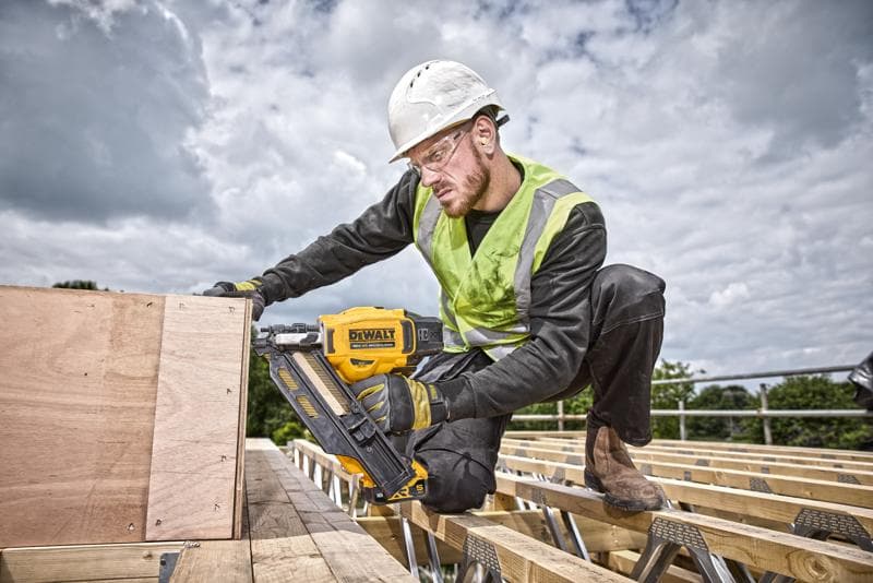 Une personne utilise un cloueur DEWALT DCN930N sur des planches en bois, sur un chantier extérieur, avec équipement de