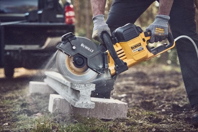Scie DEWALT coupant du béton dehors, opérateur portant des gants pour sécurité.