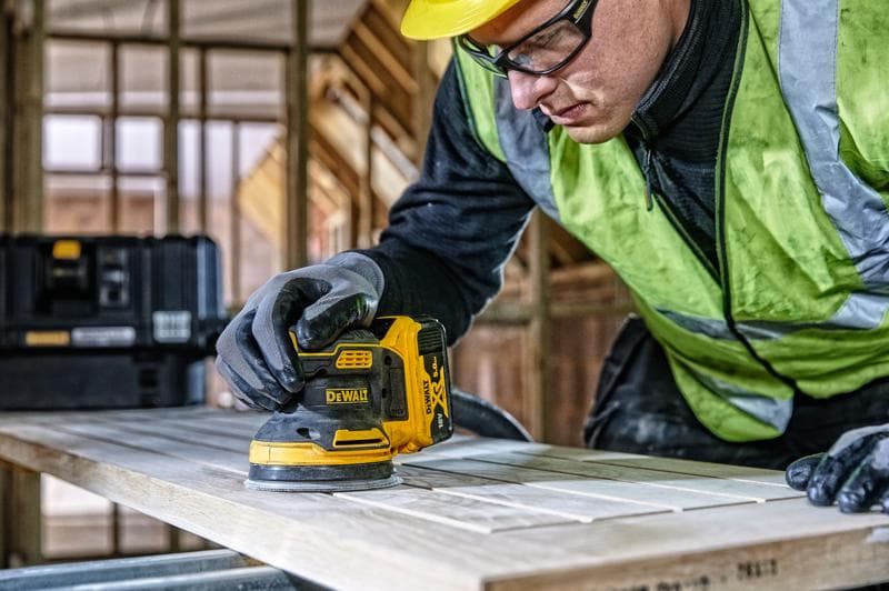 DEWALT DCW210, DCW210D1 ponceuse utilisée sur bois au chantier. Personne avec gants et gilet de sécurité.