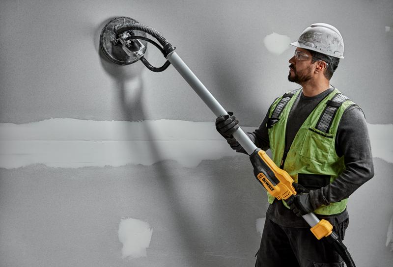 Ouvrier avec ponceuse murale DEWALT DWE7800, DWE7800-QS sur plaque de plâtre. Produit de photographie.