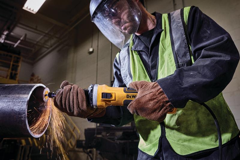 Opérateur utilisant une meuleuse DEWALT pour couper un tuyau en métal avec des étincelles, équipé de sécurité.